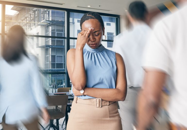 Busy office, people and a black woman with a headache, workplace stress or burnout from chaos. Tired, corporate and an African employee with pain, anxiety or fatigue from a fast company and workers